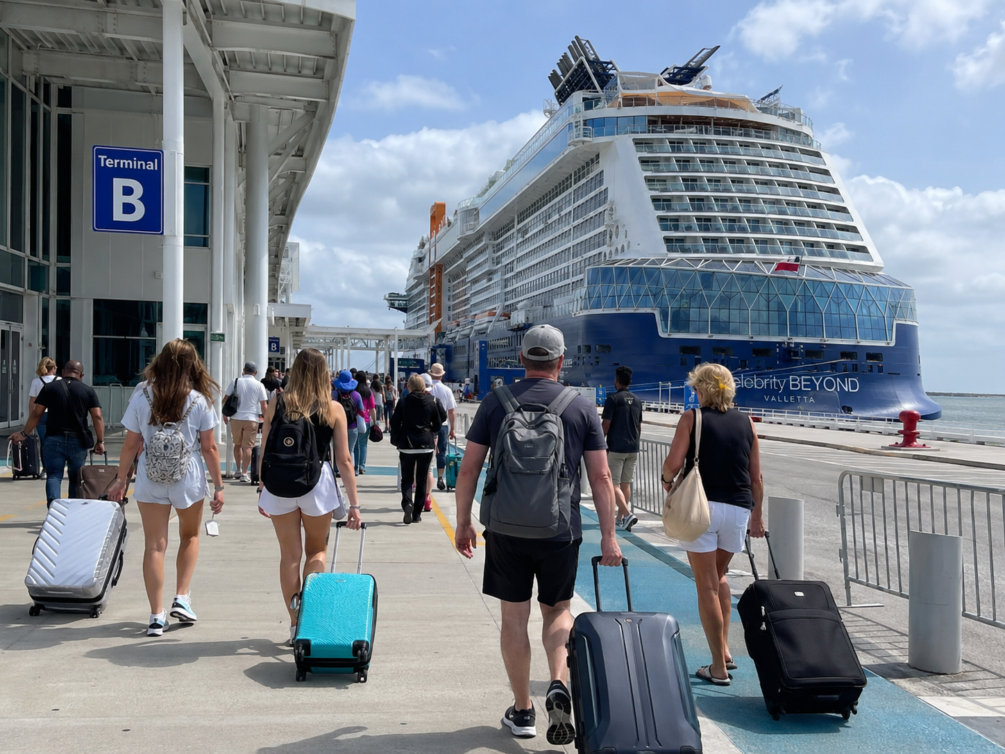 Travelers with luggage arriving at a cruise terminal as a ship waits at the pier